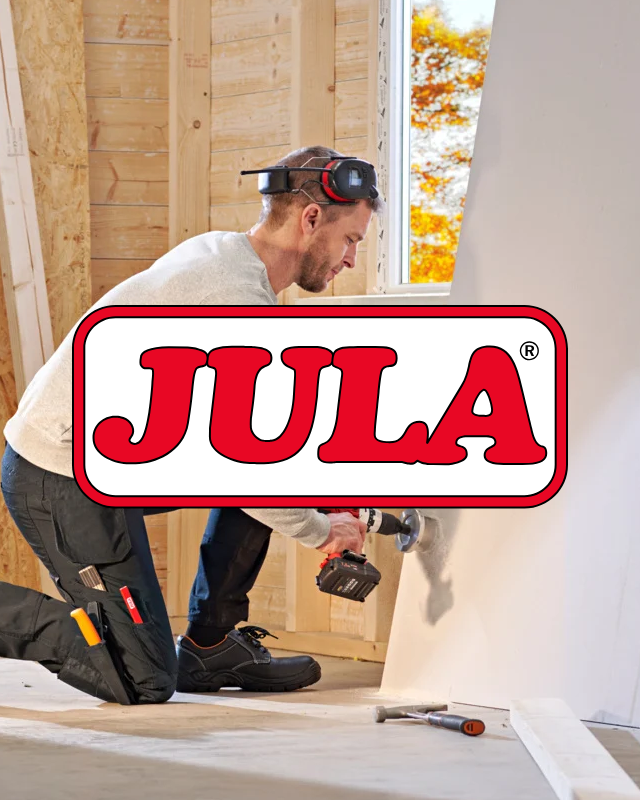 Man på knä med borrmaskin i byggmiljö, snickarklädd, JULA logotyp.